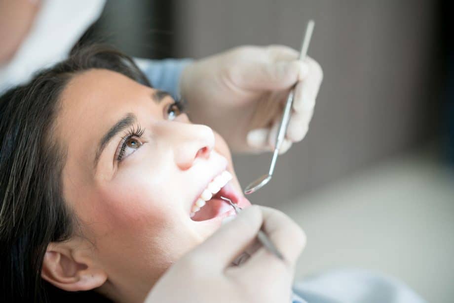 woman in dental exam chair with mouth open and dentist's holding tools above