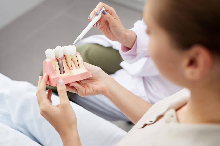 woman holding model of jaw with dental crown and implant