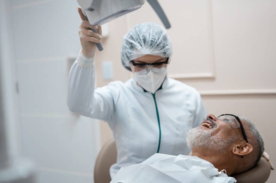 man laying back in dental chair with dental assistant holding light above